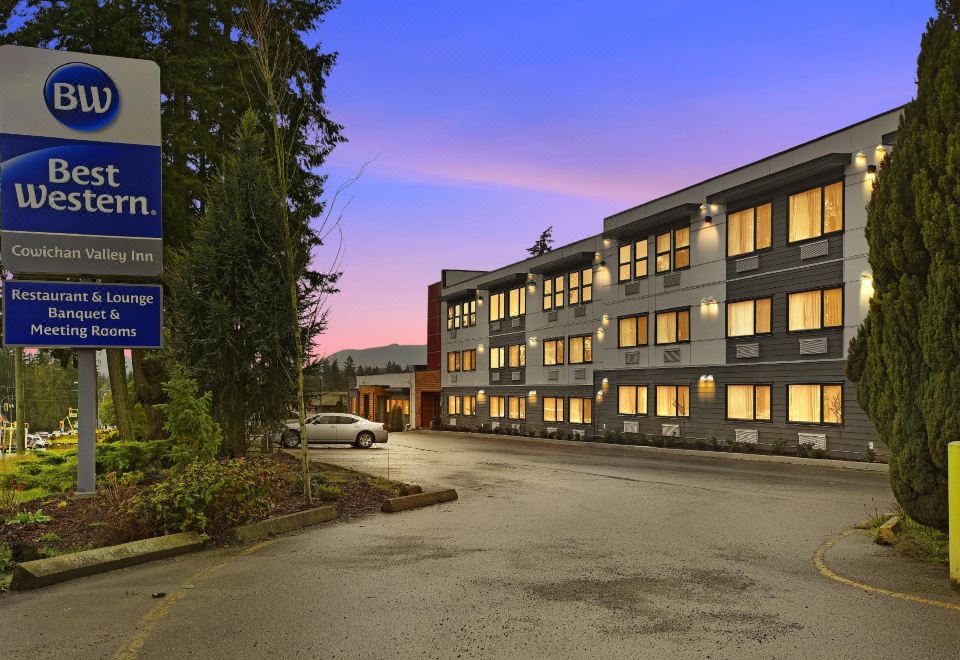 a hotel building with multiple windows and doors , surrounded by trees and a parking lot at Best Western Cowichan Valley Inn