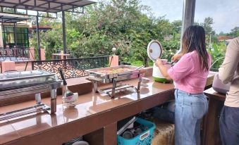 a woman in a pink shirt is standing near a dining table with a variety of dishes , preparing to serve customers at Rapeepong Resort Nanthai
