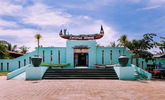 a large blue building with a boat sign on top , surrounded by palm trees and a brick walkway at Coconut Island Carita