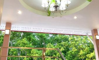 a staircase with a green chandelier hanging from the ceiling , leading to a balcony with a view of trees at P.K Inn