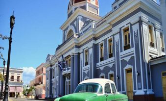 a green car is parked in front of a building with a red dome and white trim , under a clear blue sky at Hostal Oriente