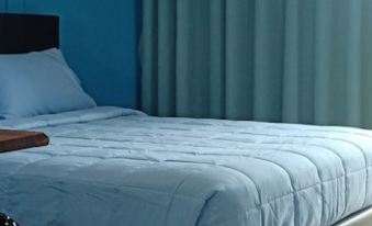 a bed with white sheets and a blue comforter is shown next to a window with green curtains at JC Resort