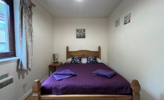 a cozy bedroom with a wooden bed , purple bedding , and a window with curtains , lit by a hanging light at River View Apartment