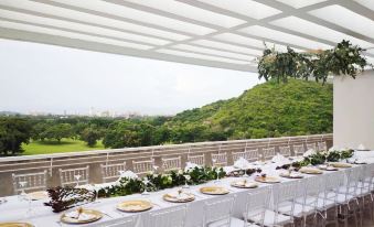 a long table with white tablecloths and gold accents is set up on a balcony overlooking a lush green landscape at Marriott Maracay Golf Resort