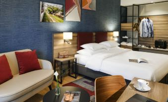 a hotel room with a comfortable bed , a flat - screen tv , a couch , and a dining table at Mercure Geneva Airport