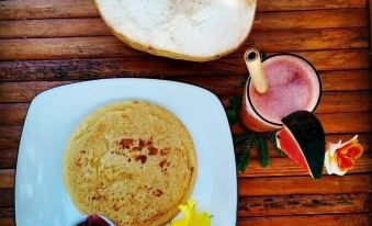 a wooden dining table with a plate of pancakes , a cup of coffee , and a bowl of jam at Rinjani Beach Eco Resort
