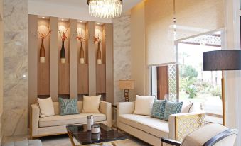 a modern living room with white furniture , a chandelier , and a large window offering views of the outdoors at Hotel Corsica & Spa Serena