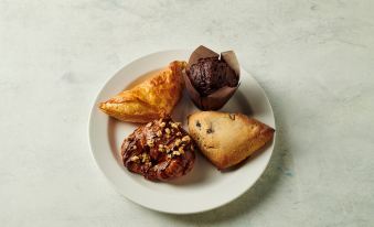 a white plate with a variety of pastries , including muffins , pastries , and pies , placed on a dining table at Holiday Inn Hammond