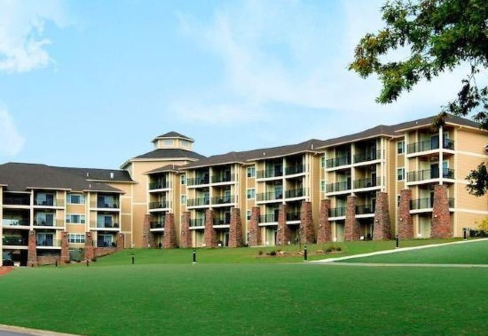 a large building with multiple floors and balconies , surrounded by green grass and trees , under a clear blue sky at Lodge of Four Seasons Golf Resort, Marina & Spa