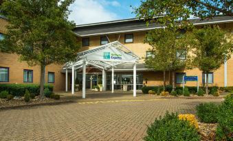 a large building with a covered entrance , possibly a hotel or a guest house , surrounded by trees at Holiday Inn Express Milton Keynes