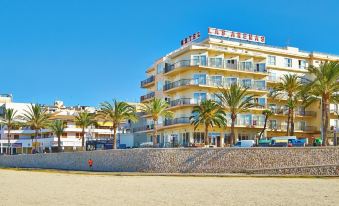 a beach scene with a large hotel building on the shore , surrounded by palm trees and a sandy beach at Hotel Las Arenas