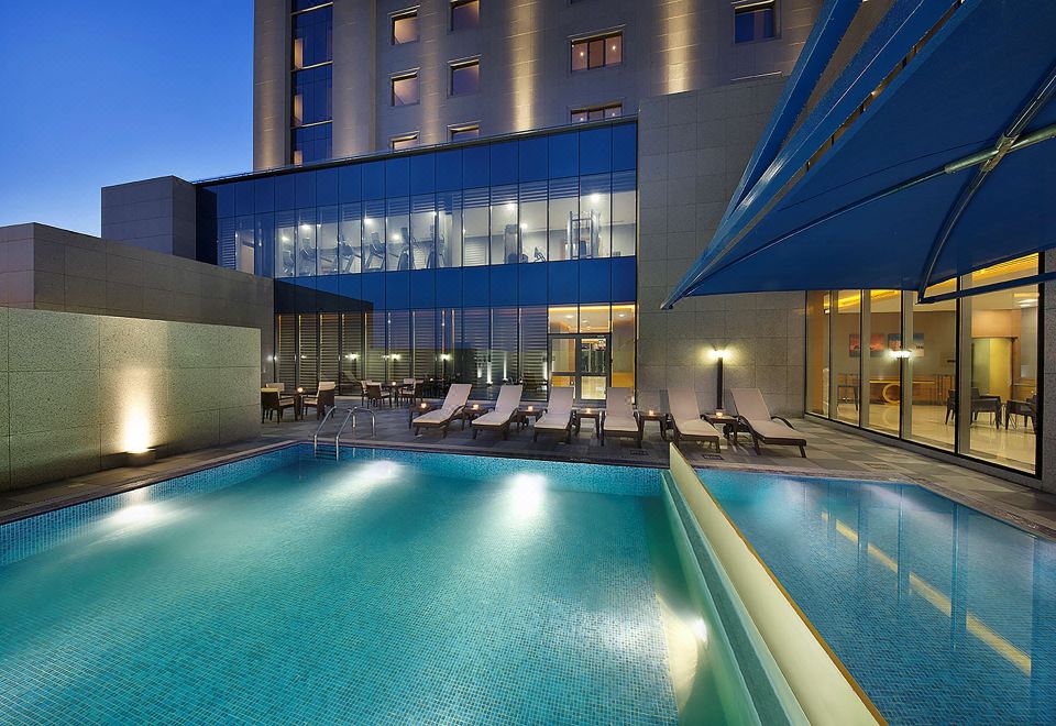 a large swimming pool with a blue awning is in front of a hotel at night at Hilton Garden Inn Tabuk