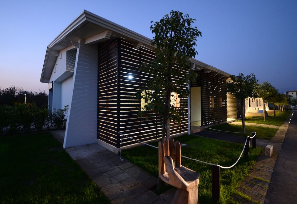 a small , modern house with a wooden fence surrounding it , situated in a grassy field at X Hotel