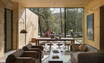 a room with a wooden table , brown chairs , and large windows overlooking a forested area at AutoCamp Yosemite