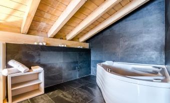 a bathroom with a white bathtub and a wooden floor , surrounded by black tiles and gray walls at Hotel Nagusi