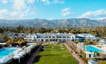 a large white building with a long lawn in front of it and mountains in the background at Rosewood Miramar Beach