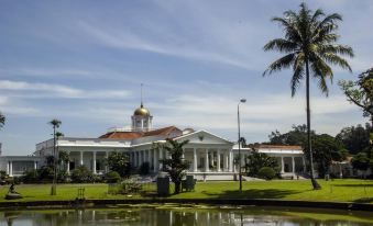 a large white building with a gold dome is surrounded by palm trees and a pond at Braja Mustika Hotel Bogor