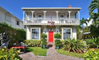 a white house with a red door , surrounded by green grass and bushes , under a clear blue sky at Sabal Palm House Bed and Breakfast