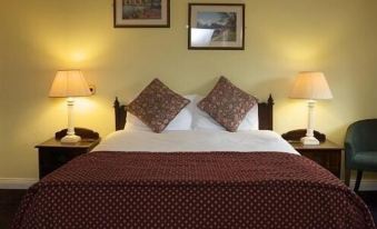 a neatly made bed with a red blanket and two lamps on either side , creating a cozy atmosphere in the room at The Cook and Barker Inn