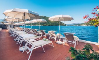 a group of lounge chairs and umbrellas on a dock , with the ocean visible in the background at Heritage Grand Perast by Rixos