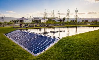 a large , open - air solar field with a water treatment plant in the center and a building with a tiled roof in the background at L'And Vineyards