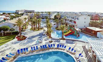 a large swimming pool is surrounded by blue lounge chairs and a white building with palm trees at Globales Los Delfines