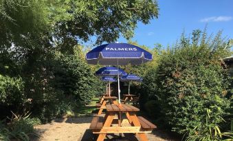 a wooden picnic table with a blue umbrella and two wooden benches under a tree at Phelips Arms