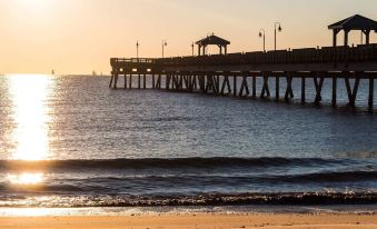 a wooden pier extending into the ocean , with the sun setting in the background and a beach visible in the distance at Victoria Hotel