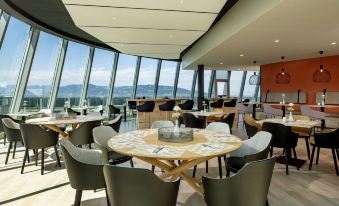 a modern restaurant with a large dining area and a view of the ocean through a window at Four Points by Sheraton Panoramahaus Dornbirn