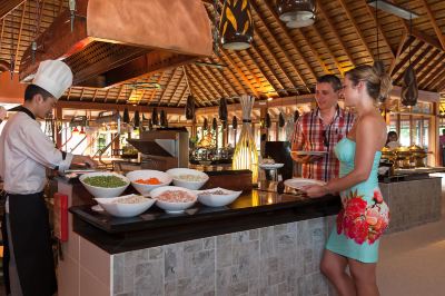 a man and a woman are standing in front of a buffet table filled with various food items at Vilamendhoo Island Resort & Spa