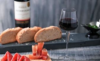 a wine glass filled with red wine next to a plate of sliced meat and bread , accompanied by olives and a bottle of wine at Amazonia Palmela Apartamentos Turisticos