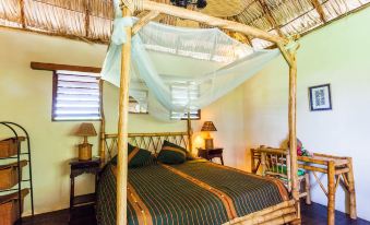 a cozy bedroom with a bamboo canopy bed , white bedding , and a tropical atmosphere at Hotel Punta Teonoste