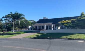 a white house with a black roof , situated on a street with palm trees in the background at Ulladulla Motel