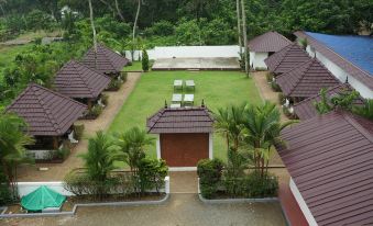 aerial view of a row of buildings with thatched roofs surrounded by lush greenery , including palm trees and greenery at The Palms Hotel