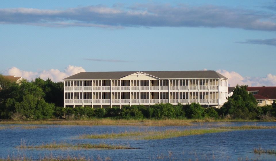 a large white building situated on the edge of a body of water , surrounded by trees and grass at The Sunset Inn