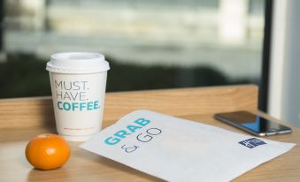"a wooden table with a cup of coffee , an orange , and a piece of paper that says "" must have coffee "" on it" at Holiday Inn Express Stevenage