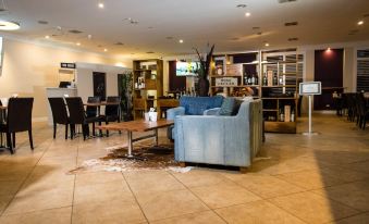 a modern lounge area with a blue couch , coffee table , and various dining furniture in a spacious room at Wattle Grove Motel