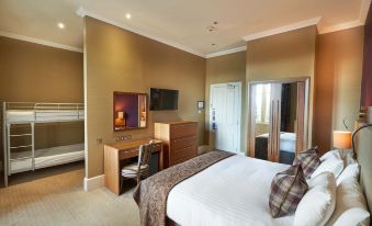 a large bed with a plaid blanket is in the middle of a room with a desk and television at Crieff Hydro