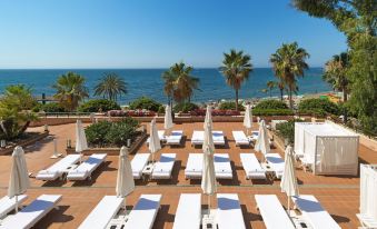 a resort with white lounge chairs and umbrellas on a patio overlooking the ocean , creating a serene atmosphere at El Fuerte Marbella