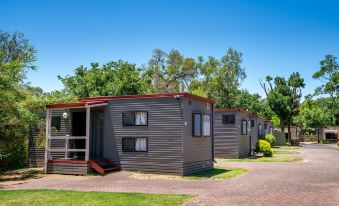 a row of small , gray mobile homes with red roofs situated in a grassy field at Adelaide Caravan Park - Aspen Holiday Parks