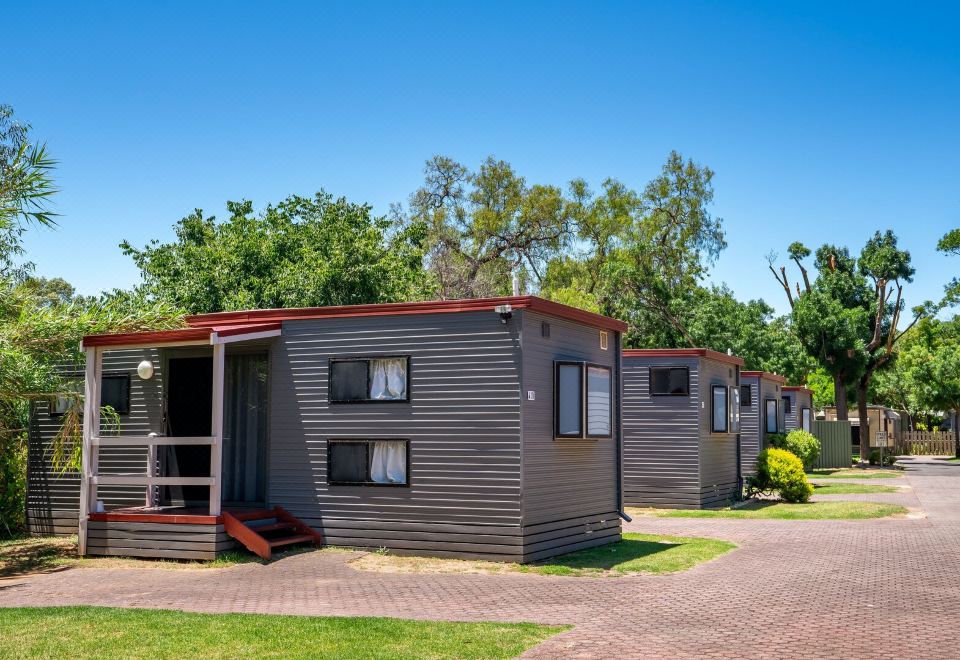 a row of small , gray mobile homes with red roofs situated in a grassy field at Adelaide Caravan Park - Aspen Holiday Parks