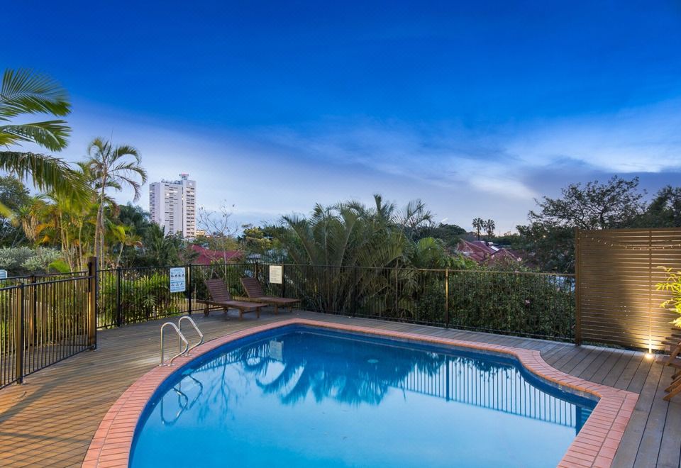 a large , curved swimming pool with clear blue water and palm trees surrounding it , under a clear blue sky at The Wellington Apartment Hotel