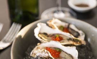 a dining table with a plate of oysters on ice , accompanied by a wine glass and a bottle of wine at The Pearl South Pacific Resort