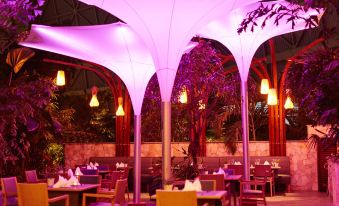 a restaurant with tables and chairs , a purple light fixture in the ceiling , and trees outside at Tropical Islands