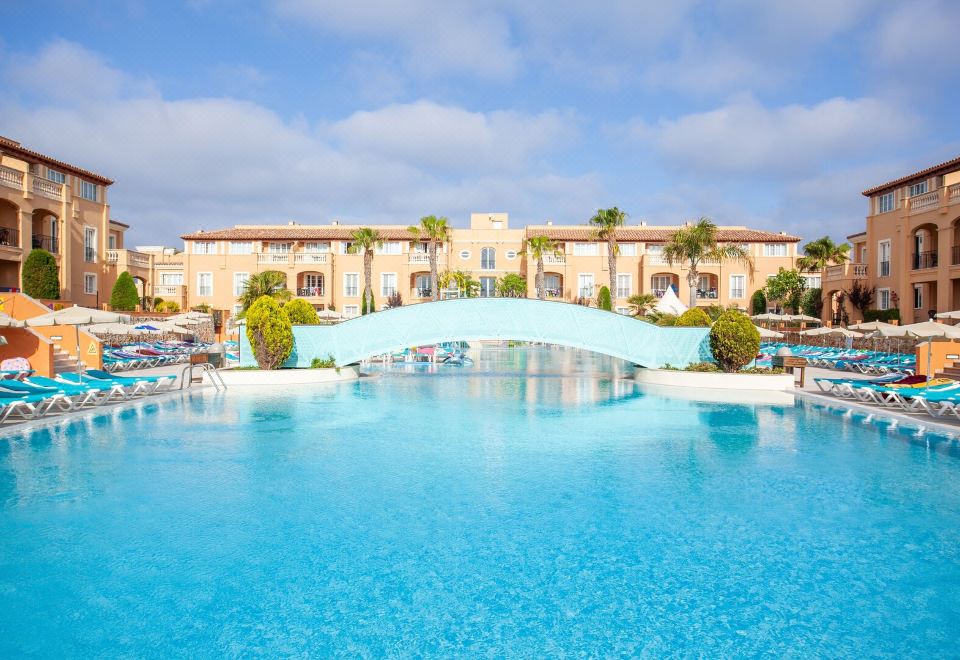 a large swimming pool with a blue bridge in the middle and a building behind it at Grupotel Club Turquesa Mar