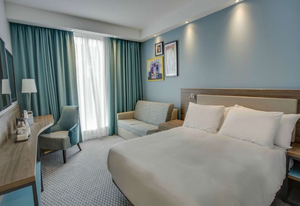 a modern hotel room with blue walls , white bedding , and a comfortable bed , along with a window and couch at Hampton by Hilton  Edinburgh Airport