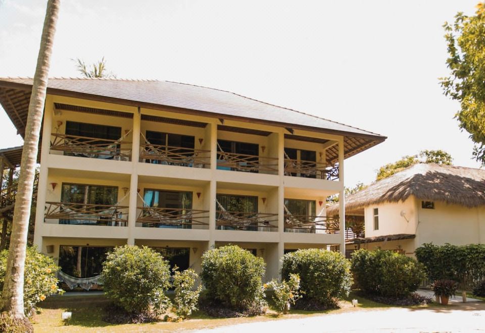 a large building with multiple floors and balconies , surrounded by trees and other buildings in the background at Pousada Praia Dos Carneiros