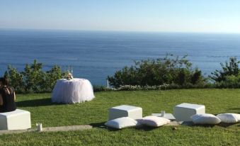 a person is standing in a grassy area with white bean bags and table settings overlooking the ocean at Villa Riviera Resort