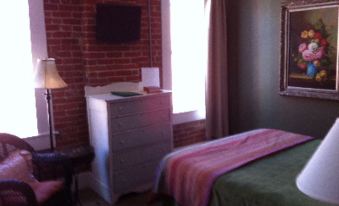 a cozy bedroom with a brick wall , a wooden dresser , and a tv mounted on the wall at William Watson Hotel