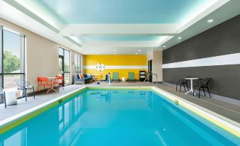 a large , empty swimming pool with blue water and yellow walls , surrounded by chairs and tables at Home2 Suites by Hilton Easton